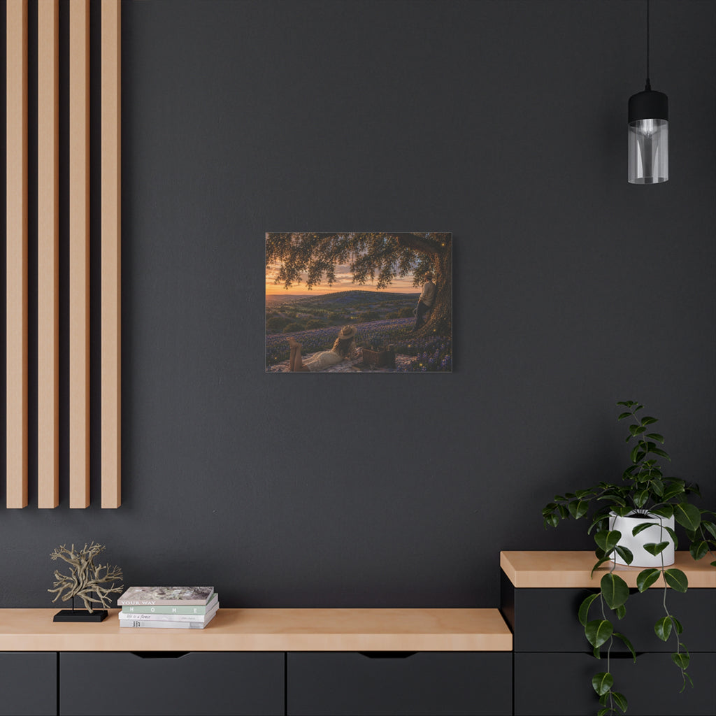 A framed wall art print depicting a sunset landscape with purple lavender fields and a tree, displayed on a white wall above a console table with a vase of white flowers, books, a small decor object, and a yellow lamp.