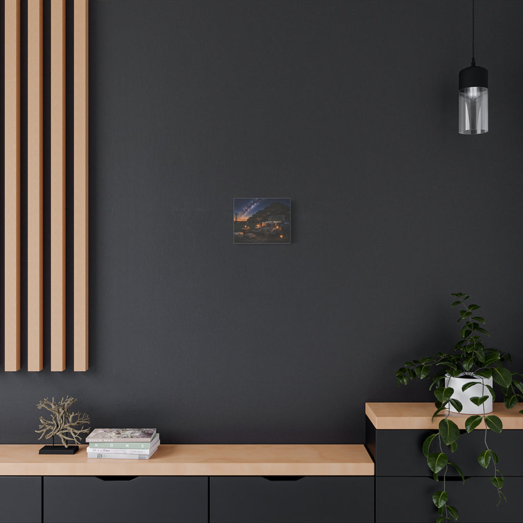 A Starry Night canvas print showing a cozy outdoor bed beside a vintage pickup in a country field, with lanterns, pillows, blankets, windmills, and the Milky Way overhead, displayed on a dark wall above wooden shelves with a plant and decor.