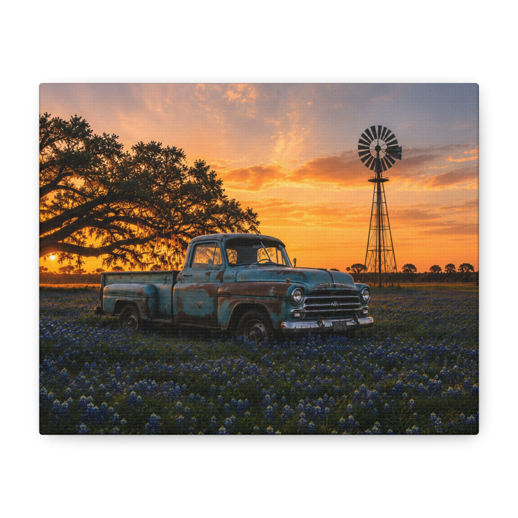 A The Windmill canvas print showing a weathered blue vintage pickup in a field of bluebonnets at sunset, with a windmill and large oak tree in the background, displayed on a dark wall above wooden shelves with a plant and decor.