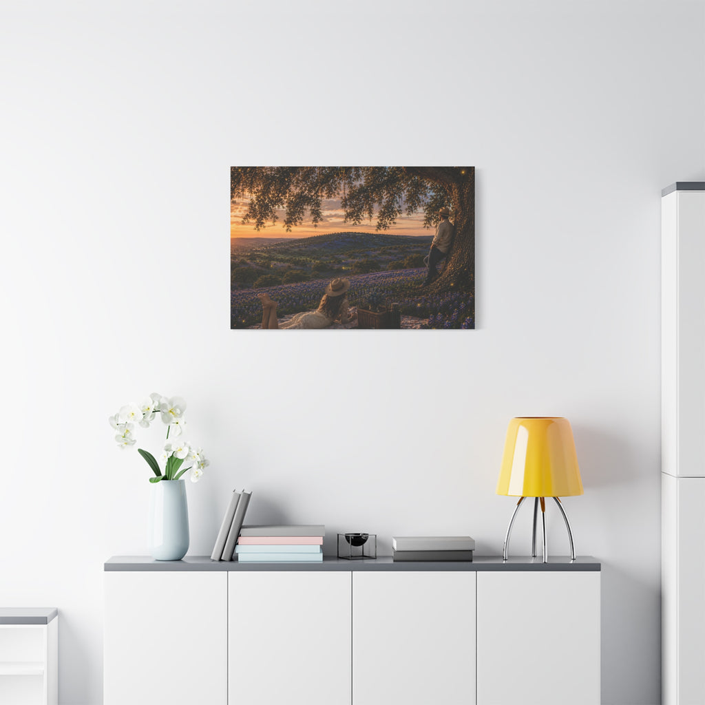 A rectangular canvas wall art print showing a romantic outdoor landscape at sunset, with a large tree, rolling hills covered in blue flowers, and two people sitting and standing under the tree. The canvas is photographed at a slight angle against a plain white background.