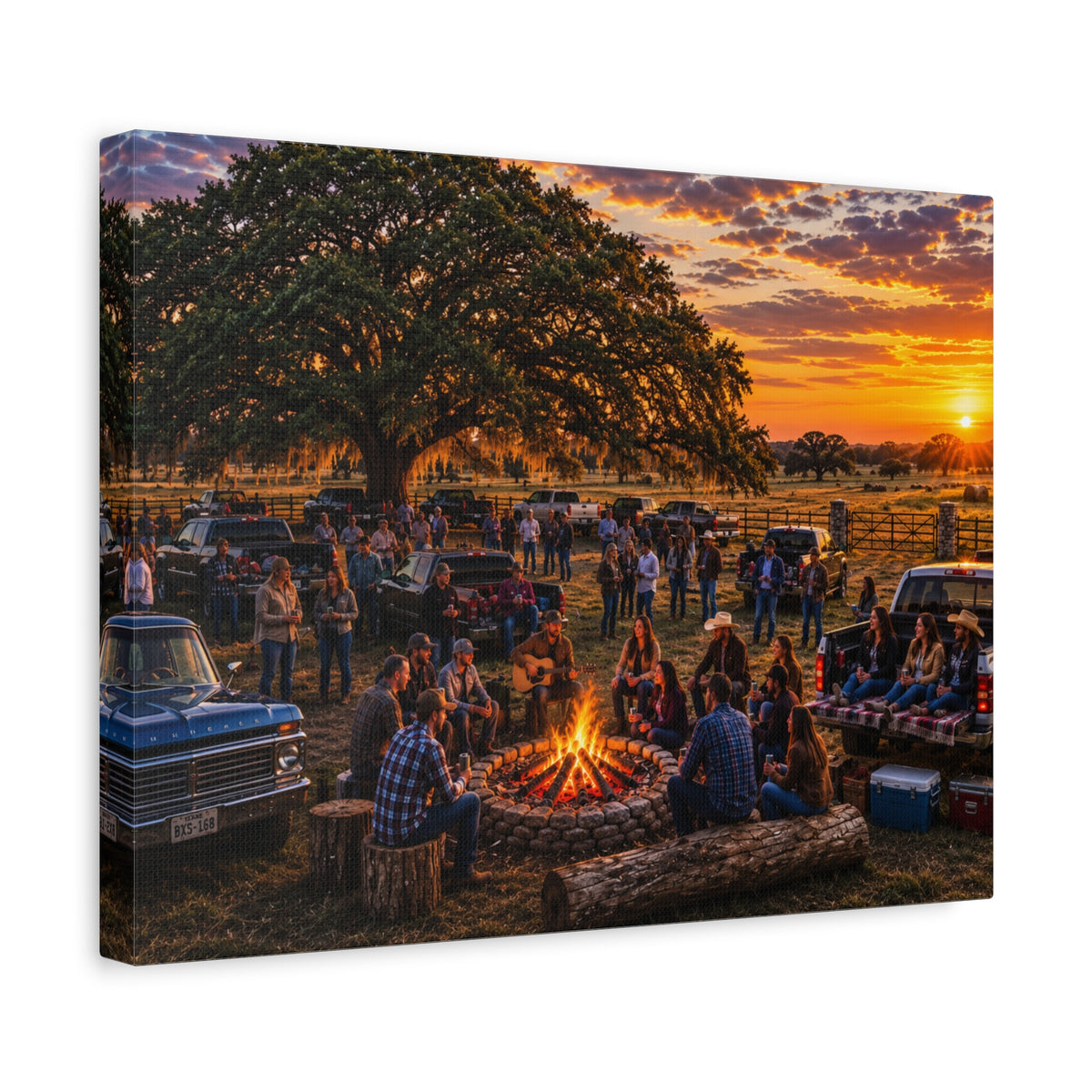 A rectangular canvas wall art print showing a rustic outdoor campsite at sunset, with people gathered around a fire pit under a large tree, parked trucks, and a warm orange sky. The canvas is photographed at an angle against a plain white background.