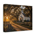A square The Country Church canvas print showing a small white country church with a steeple beside a dirt path, framed by moss-draped oak trees, rustic benches, wildflowers, and warm sunset light, photographed at an angle on a white background.