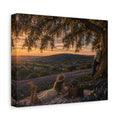 A square canvas wall art print showing a romantic outdoor sunset scene with two people under a large tree among purple flowers, photographed against a plain white background.