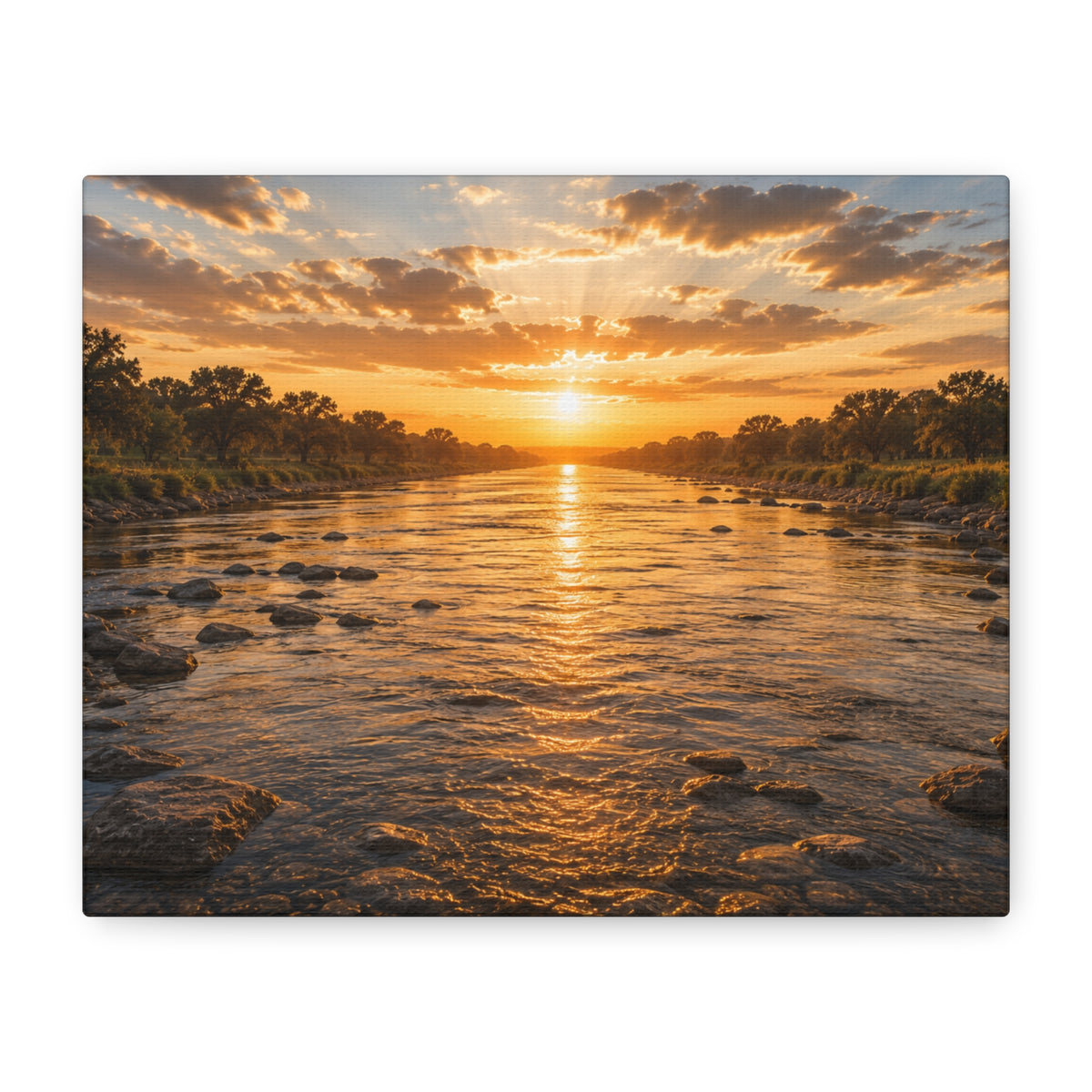 A square The River canvas print showing a golden sunset over a shallow river, with rocks in the water, tree-lined banks, glowing reflections, and sunbeams breaking through the clouds, displayed on a white wall above books and a yellow lamp.