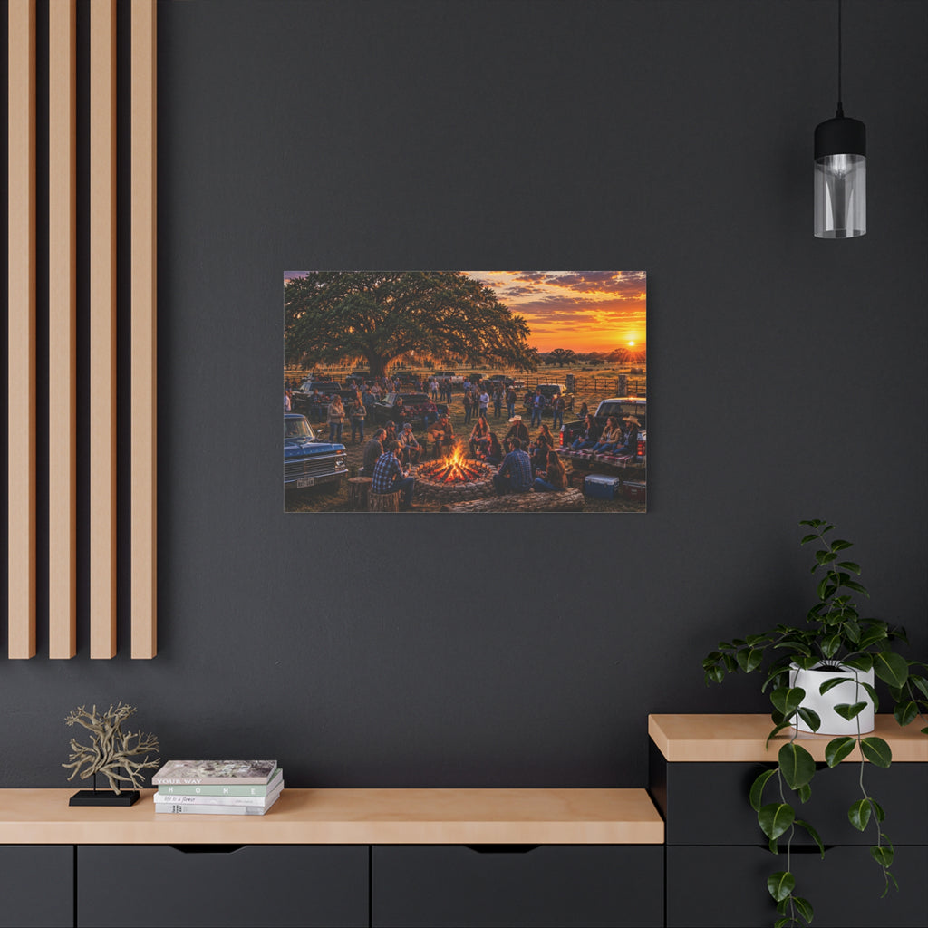 A rectangular Campfire Stories canvas print showing people gathered around a ranch campfire beneath a large oak at sunset, displayed on a dark charcoal wall above a light wood console with books, a plant, and decorative objects.