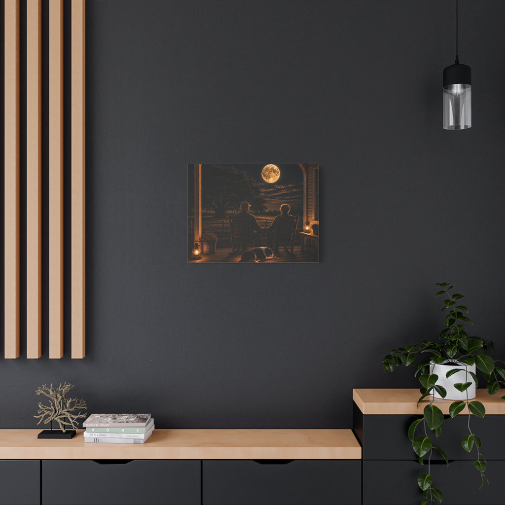 A square Harvest Moon canvas print showing an older couple holding hands in rocking chairs on a farmhouse porch with a sleeping dog, glowing lanterns, and a full moon over the fields, displayed on a dark charcoal wall above a light wood console with books and a plant.