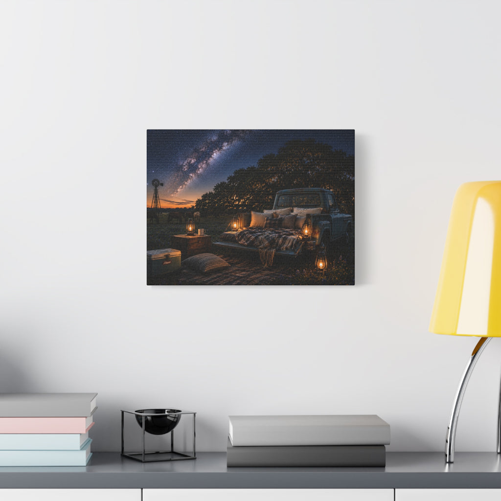 A rectangular Starry Night canvas print showing a cozy outdoor bed beside a vintage pickup in a country field, with lanterns, pillows, blankets, windmills, and the Milky Way overhead, displayed on a white wall above books, a black accent, and a yellow lamp.